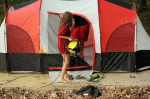 A woman carrying a fan into a camping tent.