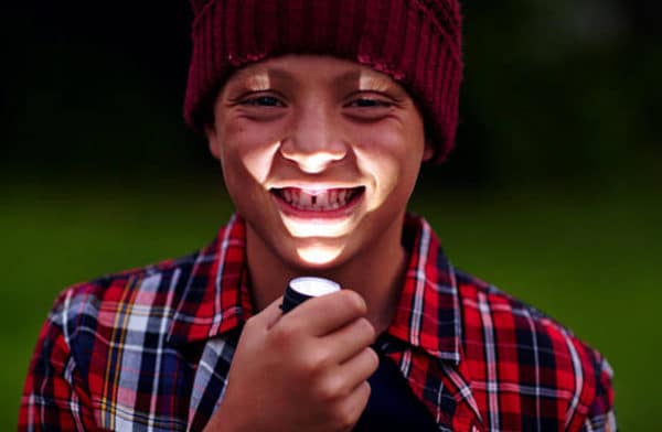 A boy using a flashlight while camping.
