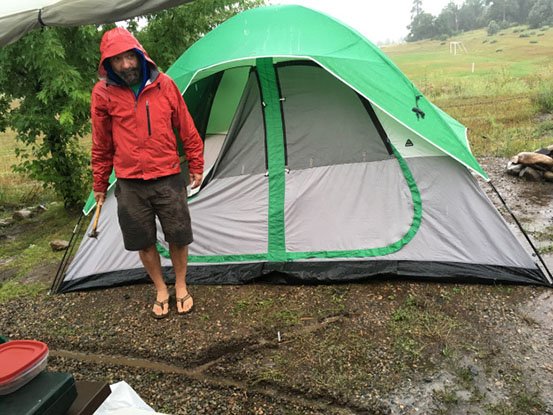 Digging a trench around a camping tent while it's raining.