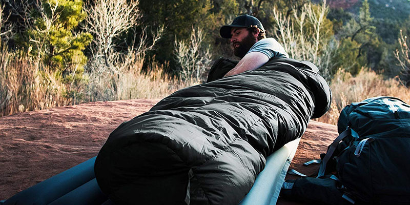 A man on a cot out in the woods camping.